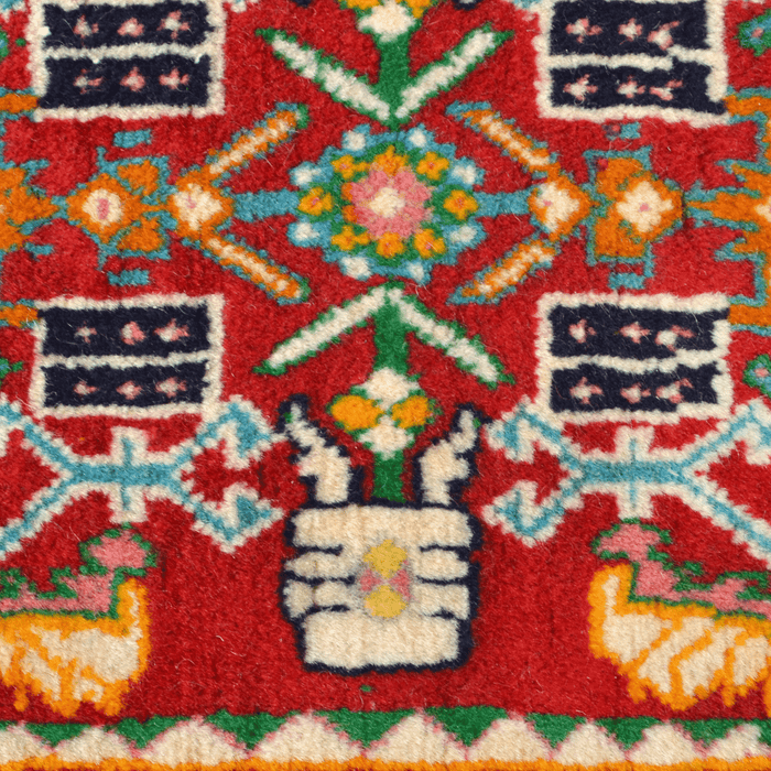 A close-up detail of a red handmade Kashkoli wool area rug, with a traditional geometric motif design. 