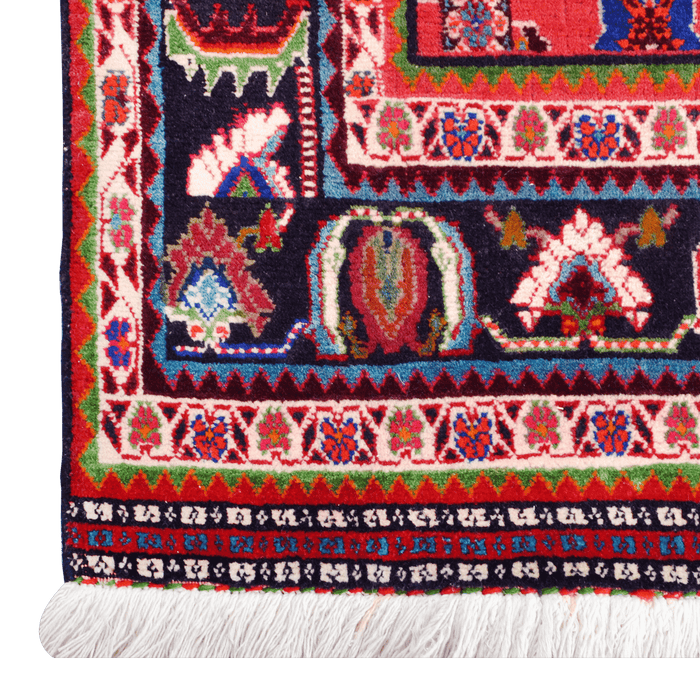 A close-up corner of a red handmade Kashkoli wool area rug, with a traditional geometric motif design. 