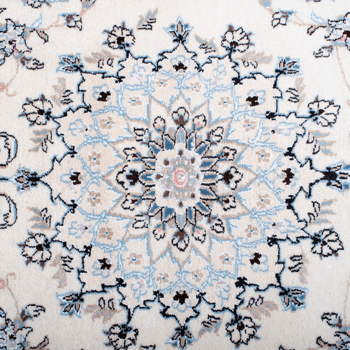 Cam Rugs: The center medallion of a cream base handmade Nain wool area rug, with accented blue details of floral motif designs. 