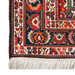 A close-up corner of a red handmade Kashkoli wool area rug, with a traditional geometric motif design. 
