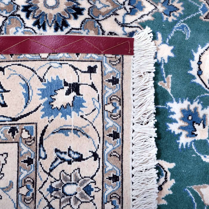 The back of a cream and green Nain wool area rug, with a traditional floral motif design.