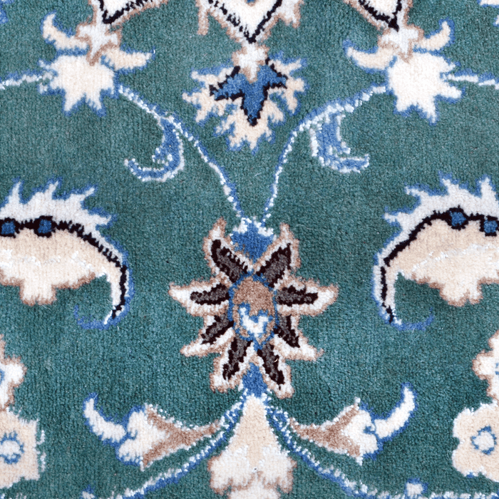 A close-up detail of a cream and green Nain wool area rug, with a traditional floral motif design.