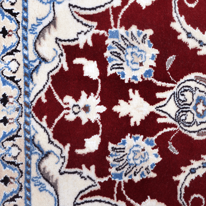 A close-up detail of a cream and red Nain wool area rug, with a traditional floral motif design.