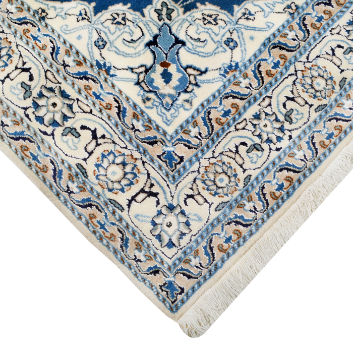 A close-up corner of a cream and blue Nain wool area rug, with a traditional floral motif design.