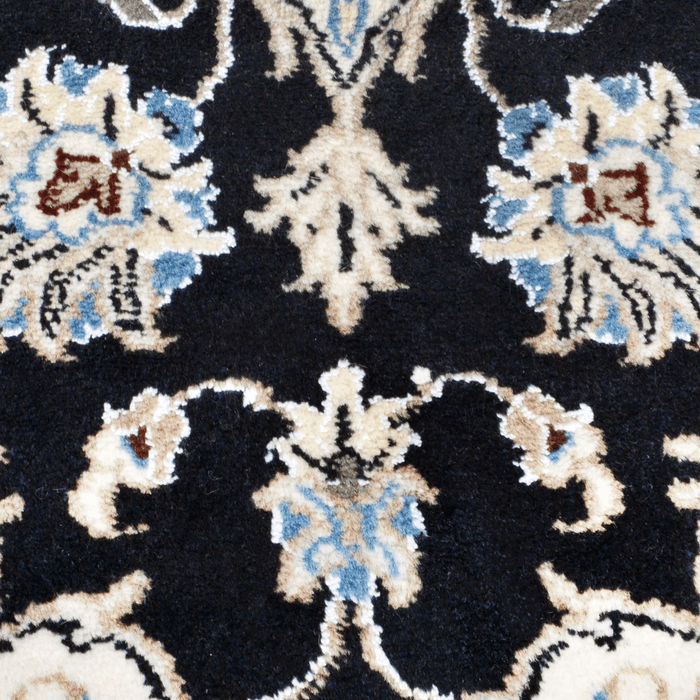 A close-up detail of a cream and black Nain wool area rug, with a traditional floral motif design.