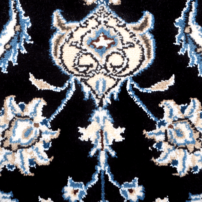 A close-up detail of a cream and black Nain wool area rug, with a traditional floral motif design.