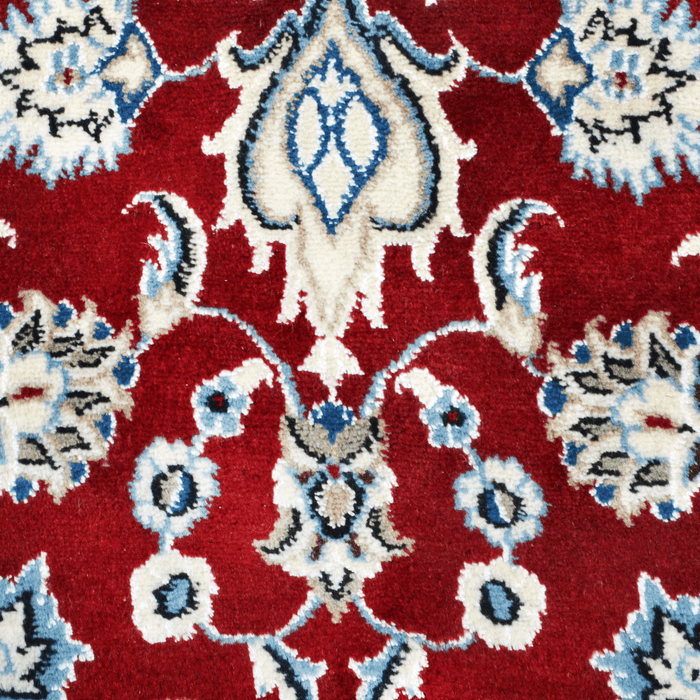 A close-up detail of a cream and red Nain wool area rug, with a traditional floral motif design.