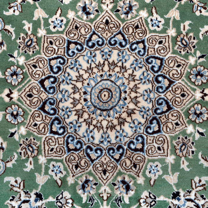 The center of a cream and green Nain wool area rug, with a traditional floral motif design.