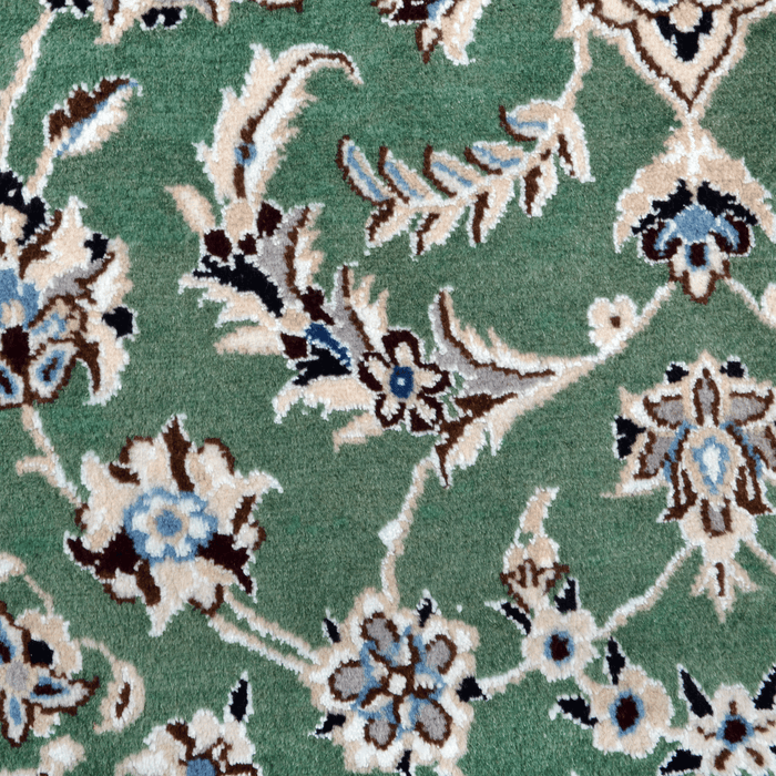 A close-up detail of a cream and green Nain wool area rug, with a traditional floral motif design.