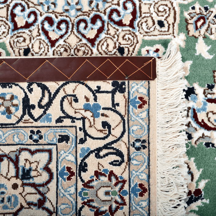 Cam Rugs: The back of a cream base handmade Nain wool area rug, with accented green details of floral motif designs. 