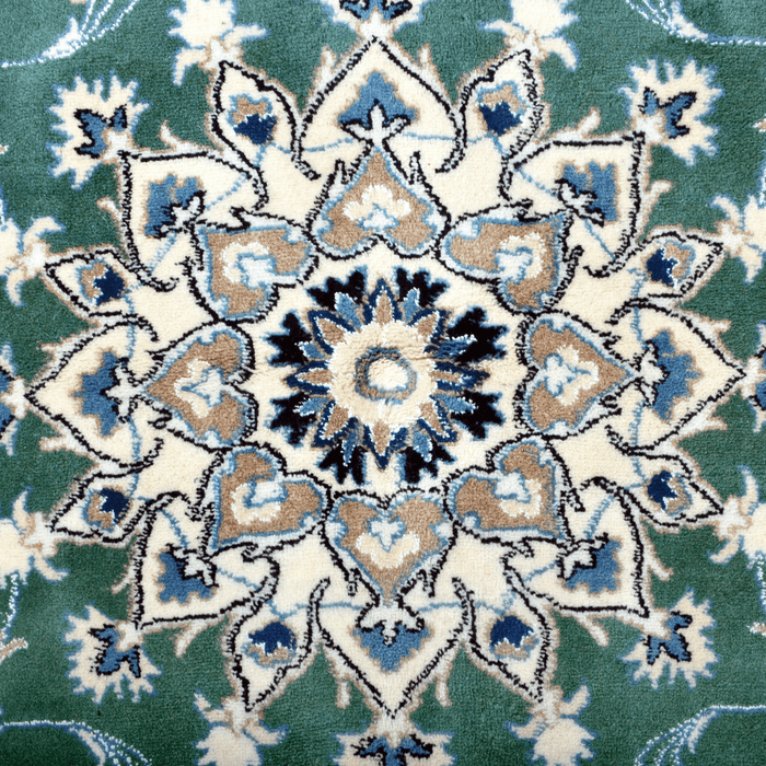Cam Rugs: The center medallion of a cream base handmade Nain wool area rug, with accented green details of floral motif designs.