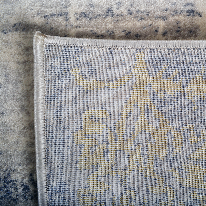 The back of a beige area rug with distressed traditional floral motifs.