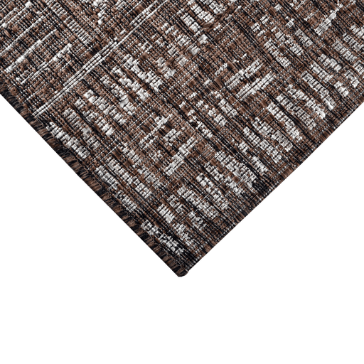 A corner of a brown flat weave outdoor rug with geometric designs.