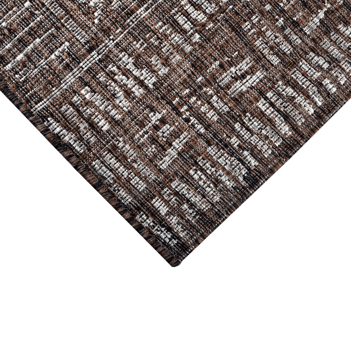 A corner of a brown flat weave outdoor rug with geometric designs.