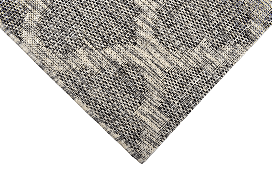 A corner of a grey flat weave outdoor rug with modern geometric designs.