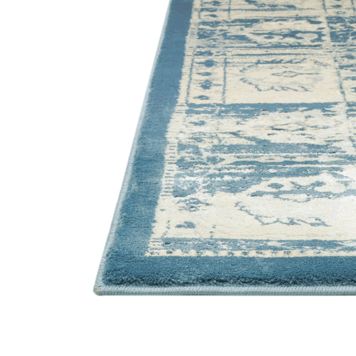 A corner of a blue and cream area rug with distressed traditional floral motif designs.
