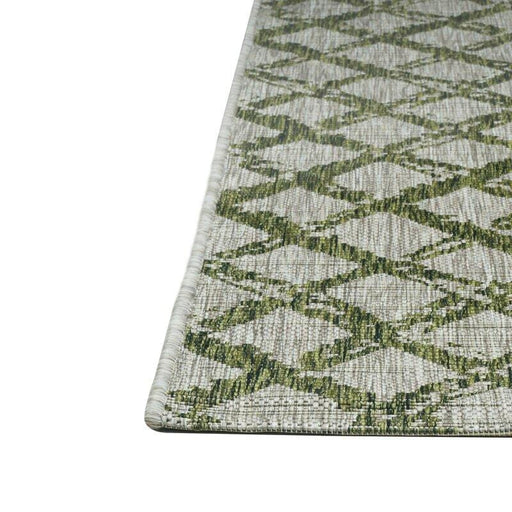 A corner of a green flat weave outdoor rug with geometric diamond designs.