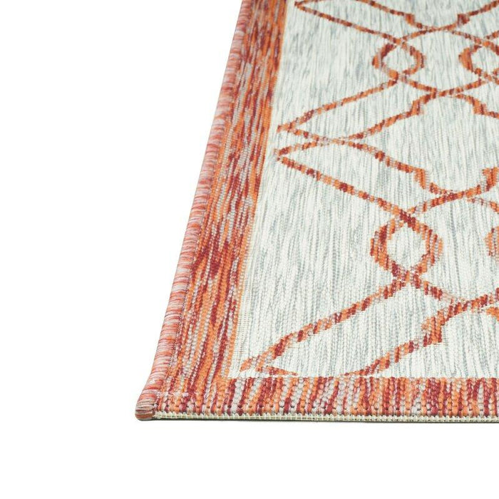 A corner of a red and grey flat weave outdoor rug with geometric designs.