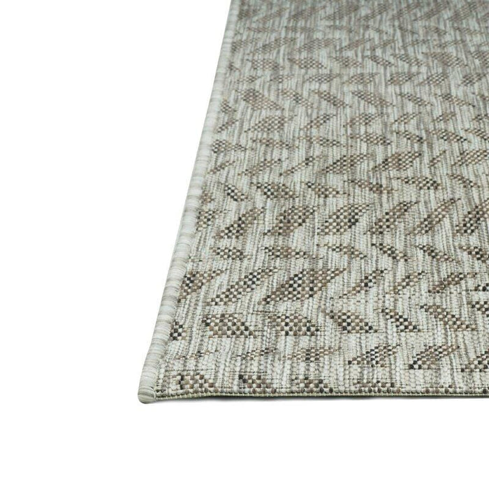 A corner of a beige flat weave outdoor rug with wavy geometric designs.
