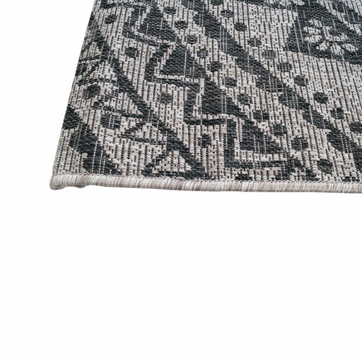 A corner of a black and grey flat weave outdoor rug with floral motif designs.