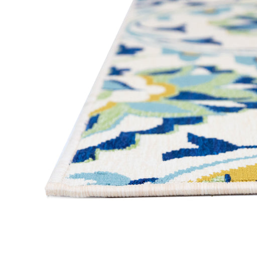 A corner of a cream area rug, with blue, green, and yellow floral damask designs.