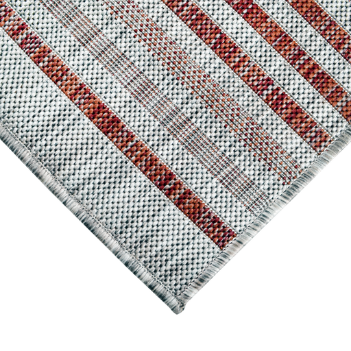 A corner of a red flat weave outdoor runner rug with striped designs.