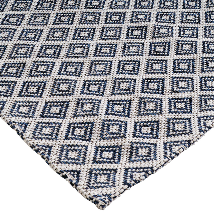 A corner of a blue flat weave area rug with geometric diamond designs.