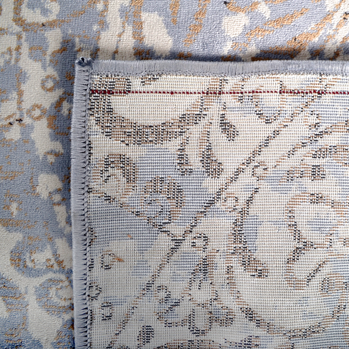The back of a blue area rug with distressed traditional floral motif designs.