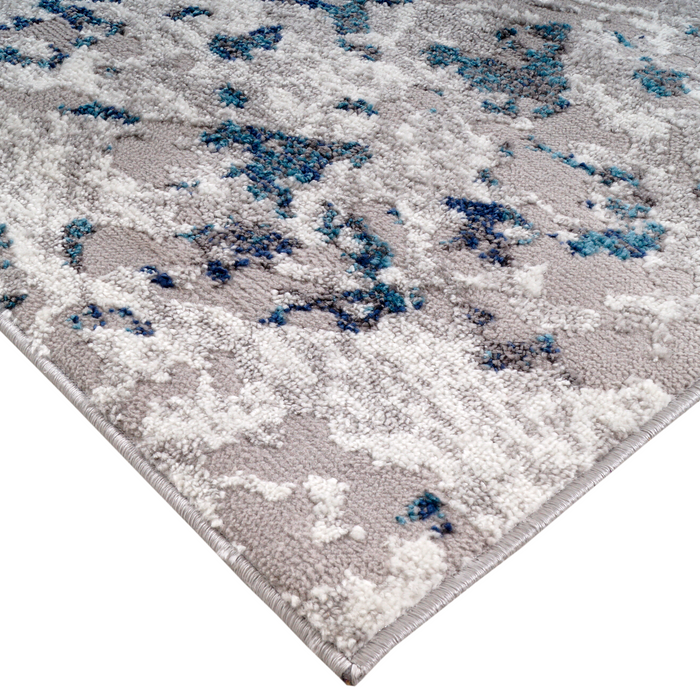 A corner of a grey and blue area rug with distressed abstract designs.