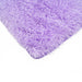 A corner of a solid lilac shag area rug.